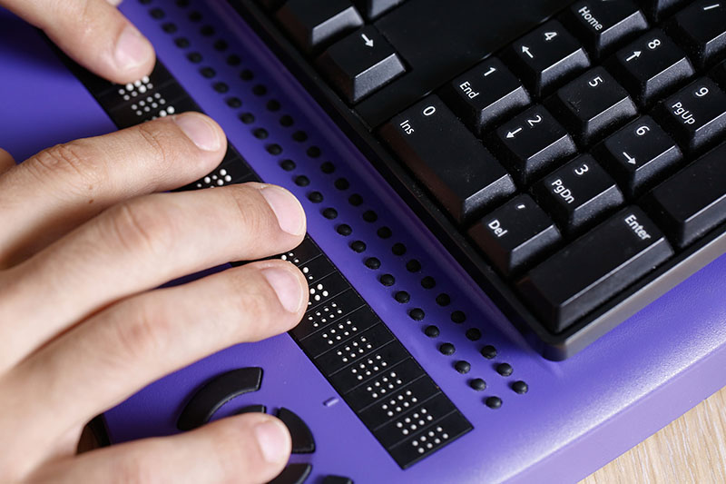 A blind person uses a computer with a braille display assistive device meant for persons with visual disabilities.