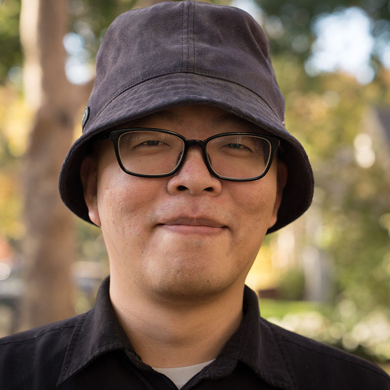 Capitol Tech Solutions web developer Che-Hung Liu smiles in a company headshot with greenery in the blurred background.