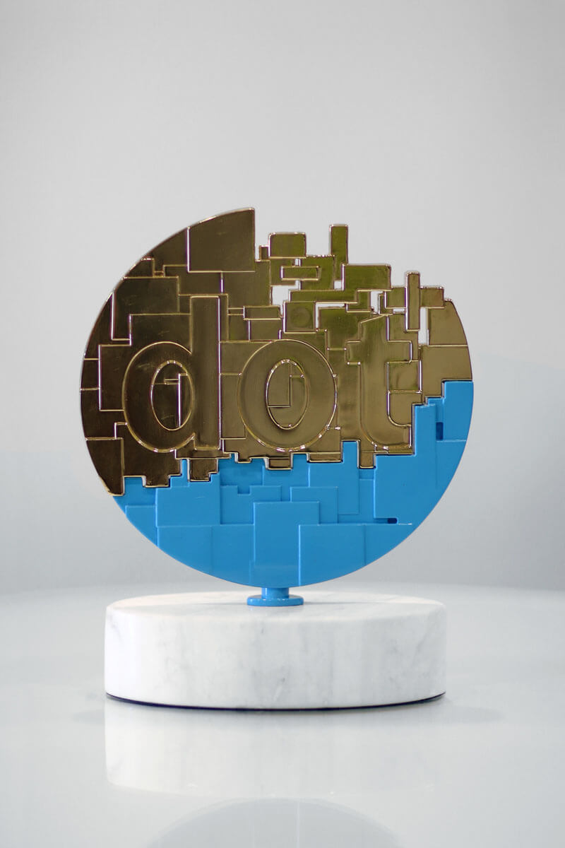 The gold dotCOMM Award is a metal cast dot broken up into individual bits. The 3-D dot sits above an oblong marble base.