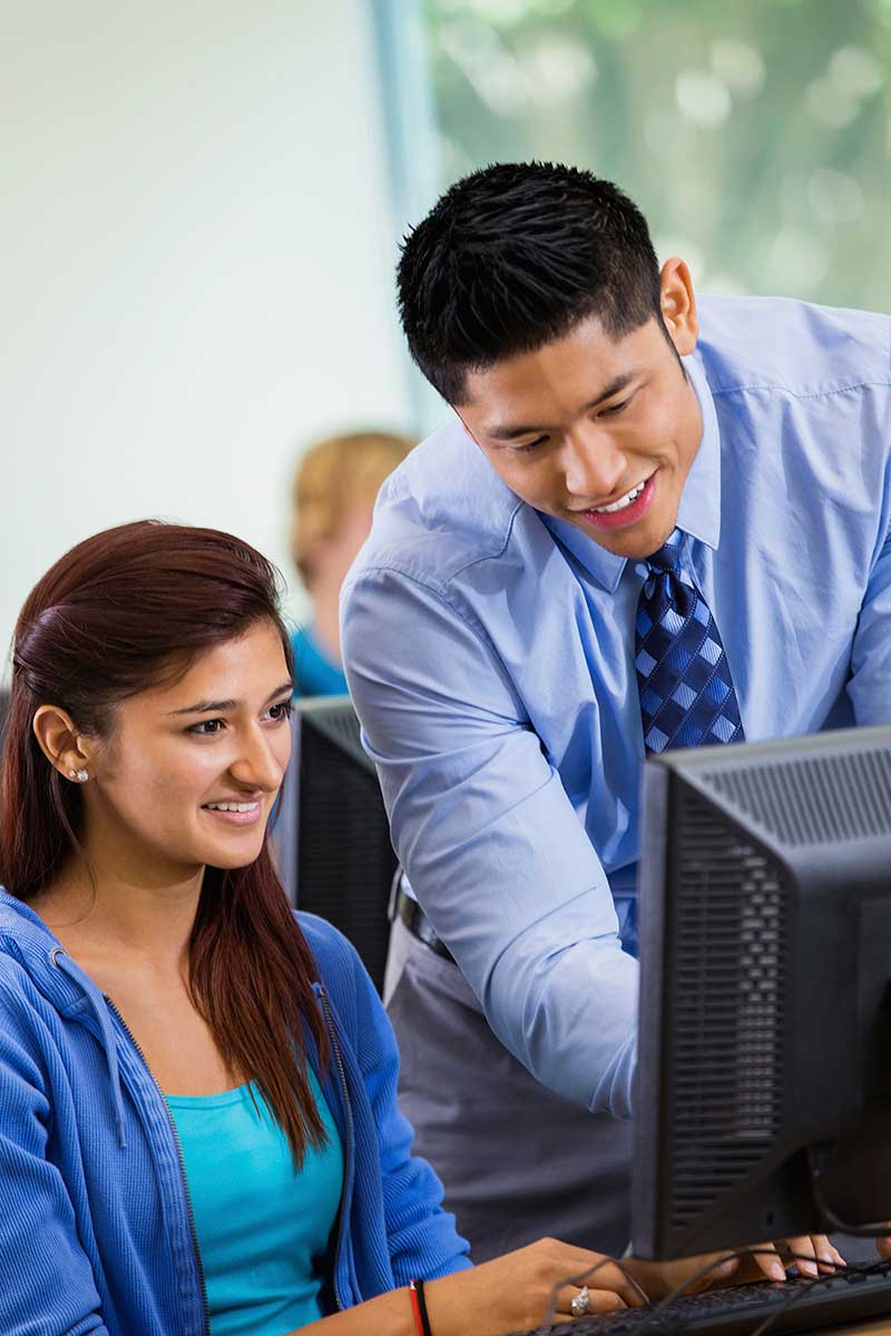 Photo of high school teacher assisting student with a computer assignment