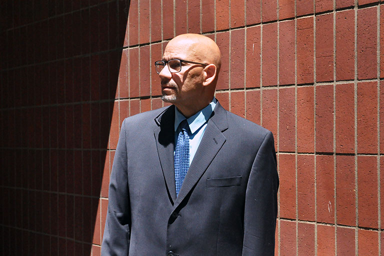 Howard Pennington wearing a suit and tie stands next to the Capitol Tech Solutions office building in Downtown Sacramento