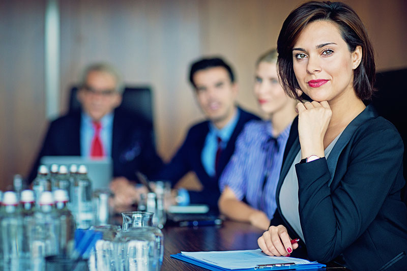 An attorney sits at a conference table during a meeting and looks at the camera