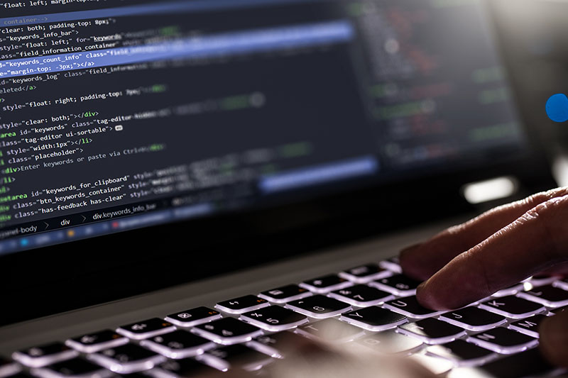 A web developer sits in front of a laptop typing HTML code to improve website accessibility for people with disabilities.